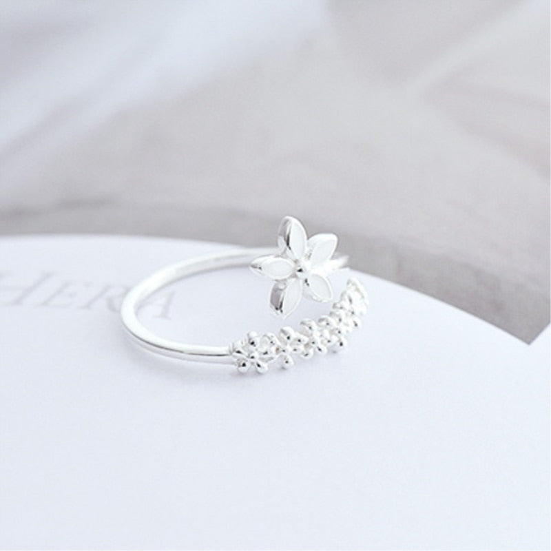 A silver ring with a floral design, displayed on a white surface.
